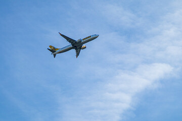 Passenger airplane in flight against a partly cloudy sky. Low angle view of a commercial jet mid-air, captured in motion with blue sky