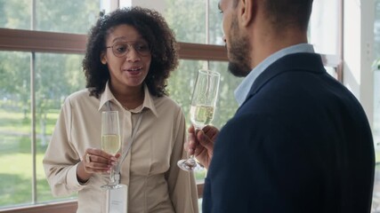 Young Black woman holding glass of sparkling wine casually chatting with her male colleague during conference afterparty
