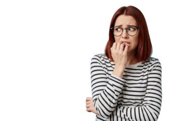 Young caucasian woman with fiery red hair, black glasses, striped shirt, biting nails anxiously in a light sky blue studio with copy space. Concept of anxiety and stress