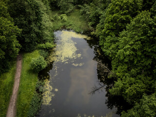 Aerial view of a dark, still pond reflects the sky, surrounded by dense, verdant trees, a narrow path tracing the edge, Vilnius, Vilnius, Lithuania.