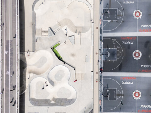 Aerial view of a vibrant skate park with winding concrete paths and a basketball court with painted logos, contrasted by the dark asphalt, Vilnius, Vilnius, Lithuania.