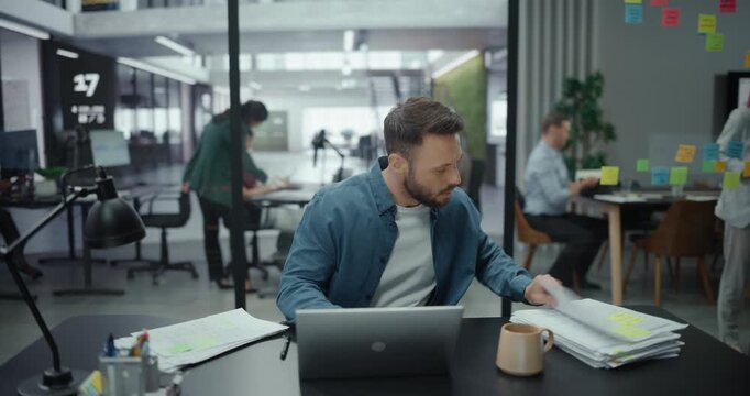 Portrait of Young Stylish Businessman Using Laptop Computer and Working with Documents and Contracts, Doing Data Analysis and Business Development. Digital Entrepreneur Works on eCommerce Project