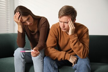 Worried couple with pregnancy test on sofa at home