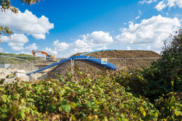 Abstract view, through a hedge of distant ground works being carried out for a new housing project in the UK. Top soil has recently been dumped on the site, as can be seen by the big mound.
