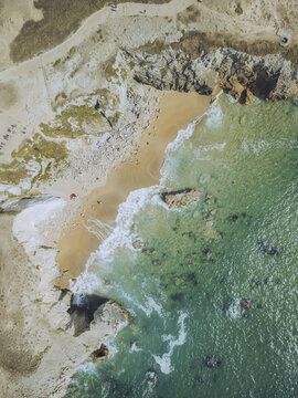 Aerial view of turquoise waters gently kissing a sandy beach hemmed in by rugged cliffs, Saint-Pierre-Quiberon, Brittany, France.