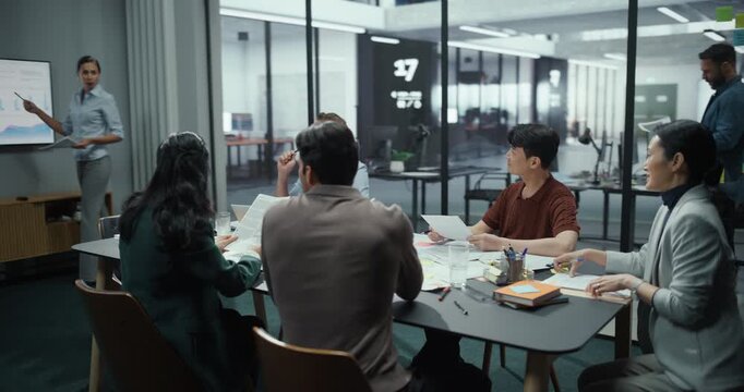Diverse Team of Business Professionals Attending a Corporate Presentation in a Modern Conference Room. Female Manager Stands in Front, Delivering a Keynote While Colleagues Listen and Take Notes