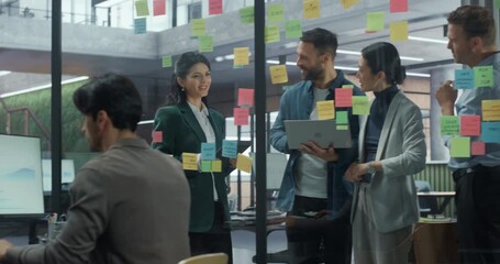 Team of Young Employees Stands by a Glass Wall in the Office, Discussing Ideas and Placing Colorful Post-it Notes to Organize a Complex Project Plan. They Collaborate Closely and Share Suggestions - Powered by Adobe