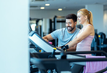 Mid adult woman and personal fitness trainer preparing for workout on treadmill at gym.