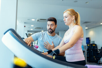Mid adult woman and personal fitness trainer preparing for workout on treadmill at gym.