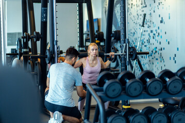 Personal fitness trainer supervising middle aged woman during gym workout with weights.