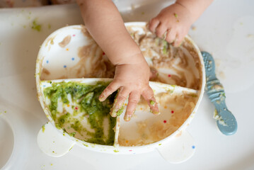 A small child eats porridge and vegetables at his table with his own spoon, his first complementary food.