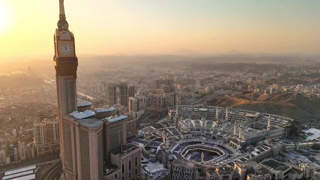 drone footage of Mecca, Saudi Arabia, filmed at sunset. The video captures the vast urban landscape with residential buildings, modern towers, and surrounding mountains bathed in golden hour light