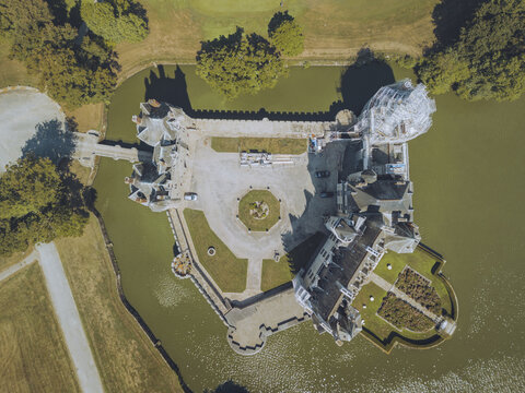 Aerial view of the Ch&Atilde;&cent;teau de la Bretesche, a medieval castle surrounded by a moat reflecting soft light, with lush trees adding a vibrant contrast, Missillac, Pays de la Loire, France.