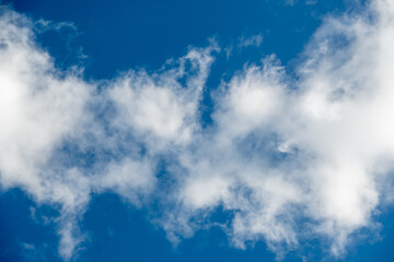 La fotografía muestra nubes blancas y suaves dispersas en un cielo azul intenso, creando una sensación de calma y tranquilidad. La luz del sol ilumina los bordes de las nubes.