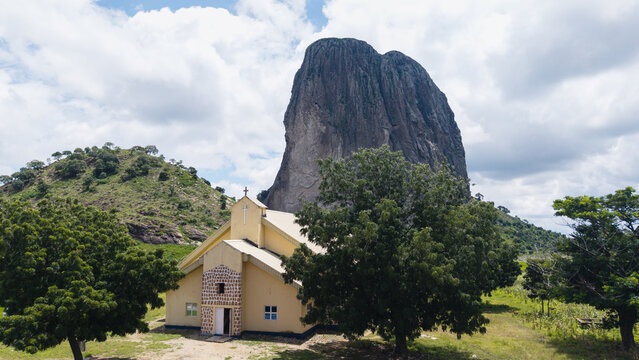 Aerial view of the imposing Wase Rock towering over a quaint church, its aged walls contrasting with the rugged landscape, Wase, Plateau, Nigeria.