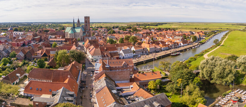 Aerial view of the serene Ribe Cathedral towering over the town's red rooftops, nestled beside a tranquil river reflecting the sky, Ribe, Denmark.