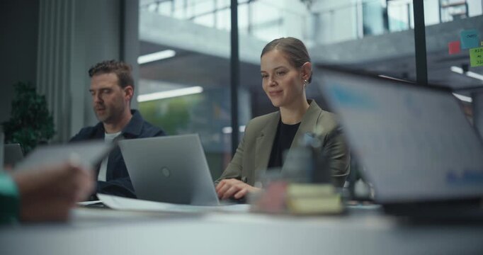 Group of Male and Female Business Professionals Sitting Around a Conference Table, Focused on Their Laptop Computers. Employees Type, Research and Collaborate Quietly in a Modern Office