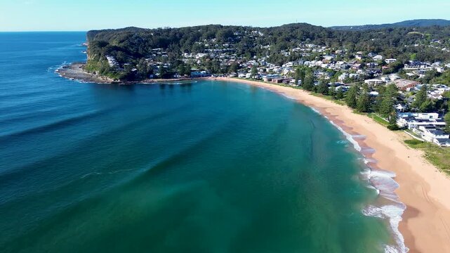 Drone aerial landscape of ocean waves breaking on shoreline of Avoca Beach town suburbs with housing and shops along headland and coastline in Central Coast New South Wales Australia travel tourism