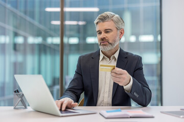 Businessman using laptop computer and holding a credit card, processing an online payment or e-commerce transaction while shopping from a modern office environment