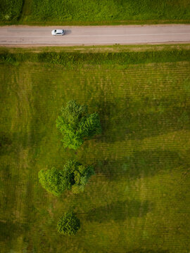 Aerial view of a lone car traversing a dirt road amidst a vibrant tapestry of green fields dotted with trees, Merkine, alininkai, Lithuania.