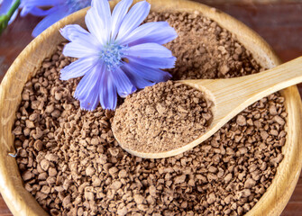 Ground chicory root on a wooden spoon and chicory flowers on a rustic wooden background. Alternative medicine. Healthy drinks. chicory drink