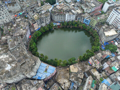 Aerial view of a serene, oval lake embraced by a ring of verdant trees amidst the dense urban sprawl of buildings, Dhaka, Dhaka Division, Bangladesh.