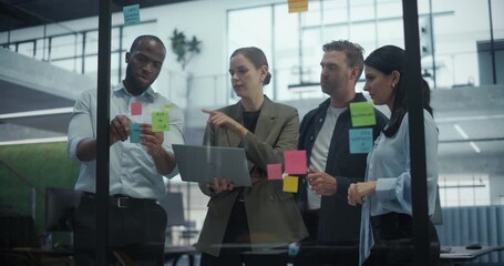 Employees Engage in a Creative Planning Session, Writing On and Placing Post-It notes on a Glass Wall to Structure a Business Project. They Discuss Each Suggestion and Rearrange Notes - Powered by Adobe