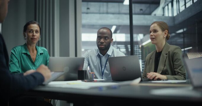 Employees Sitting Side by Side in a Meeting in Conference Room, Working on Laptop Computers and Having a Conversation. Group is Busy with Reports and Project Planning for a Corporate Client