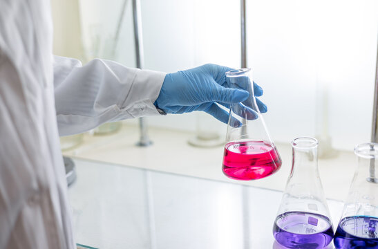 Scientist in a laboratory holding a volumetric flask containing a purple chemical. Titration analysis.