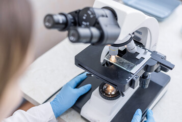 Medical science laboratory: Female biochemist looks under microscope. Scientist studying new virus in laboratory using microscope. Virology during coronavirus outbreak conducting.