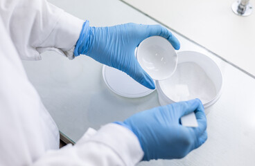 Naklejka premium A female chemist pours a reagent from a plastic jar into a porcelain bowl.