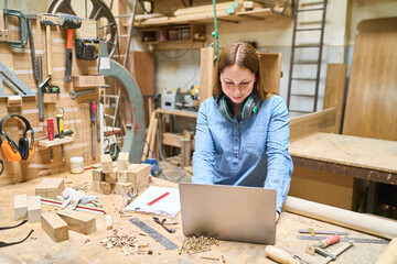 Young carpenter using laptop in a busy woodworking shop