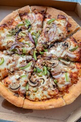 Close-up of a fresh pizza in a cardboard box topped with cheese, mushrooms, red onions, and green peppers. Concept of fast food, delivery, and casual dining at home