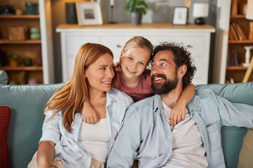 Fototapeta premium A family sits comfortably on a couch in their living room, sharing joyful moments. The parents smile at each other while their daughter beams with happiness, enhancing the atmosphere of love.