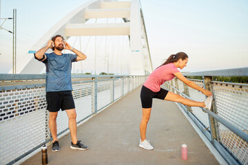 Two individuals practice stretching and warm-up routines on a bridge as the sun rises, highlighting...