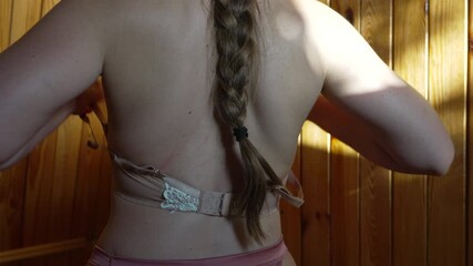 Woman removing bra from her back in a private wooden room.