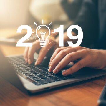 New Ideas in the Making: A person's hands diligently navigate a keyboard, overlaid with an image of a glowing light bulb, the number 2019 suggesting the dawn of fresh innovations.