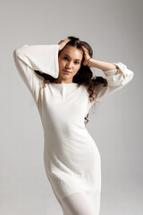 Fototapeta premium Model poses gracefully in a white knit dress with long sleeves against a plain background