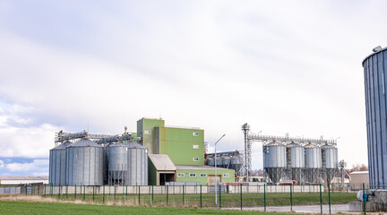 Steel grain storage silos with a conical bottom can be used for various purposes. Industrial facilities of feed and flour mills. Against the backdrop of a beautiful sky with clouds.