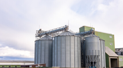 A low-angle view of large fly ash silos at an industrial plant, showcasing the towering infrastructure used for ash storage and processing. The silos are equipped with ladders and metal support struct