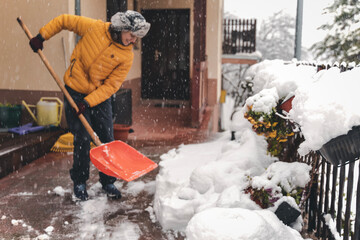 Woman cleaning snow from porch near her cottage and using snow shovel. Winter season