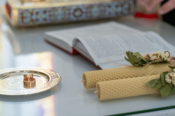 Wedding rings on a table with an open bible and candles