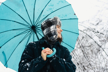 Happy woman with a blue umbrella in the snow