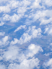 Bright blue sky dotted with fluffy white clouds over distant landscape during daytime view from above