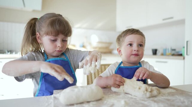 Knead dough with child and sibling girl and boy wear apron and use flour while baking together in bright kitchen learning tactile skill and playful family bonding capturing playful learning and joy