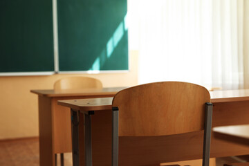 Desks with chairs and green chalkboard in classroom, selective focus