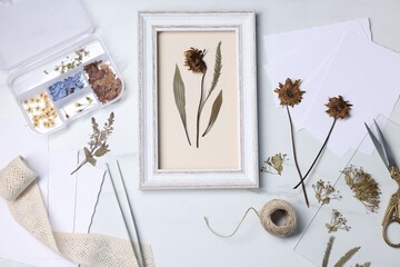 Flat lay composition with dry flowers and picture frame on white marble table