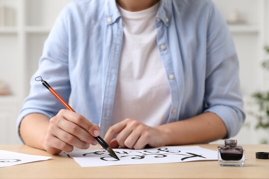 Calligraphy. Woman with brush writing phrase Keep Going on sheet of paper at wooden table indoors, closeup