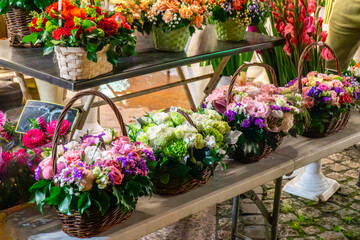 Wicker baskets with colorful flowers arranged on table at night market, decorative floral compositions with fresh plants.