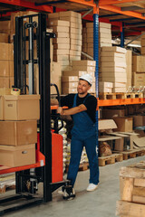 Moving stuff by using forklift. Man in uniform is working in the storage with packages for shipment